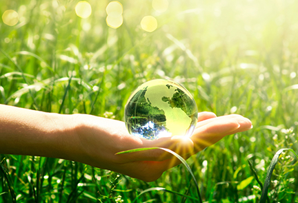 Earth crystal glass globe in human hand on grass background. Saving environment and clean green planet concept. Card for World Earth Day concept.