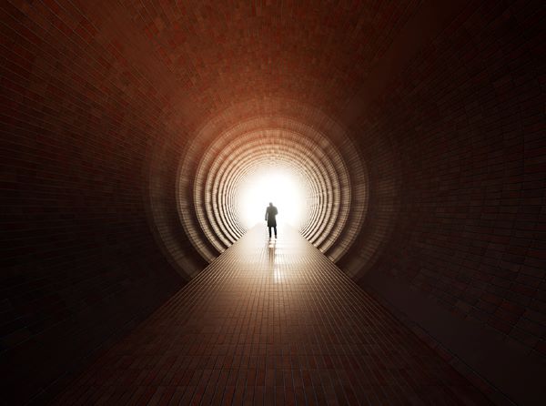 A male figure walks through a dark tunnel towards a dramatic circle of light.