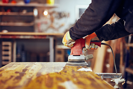 Carpenter using orbital electric sander in a retro vintage workshop.