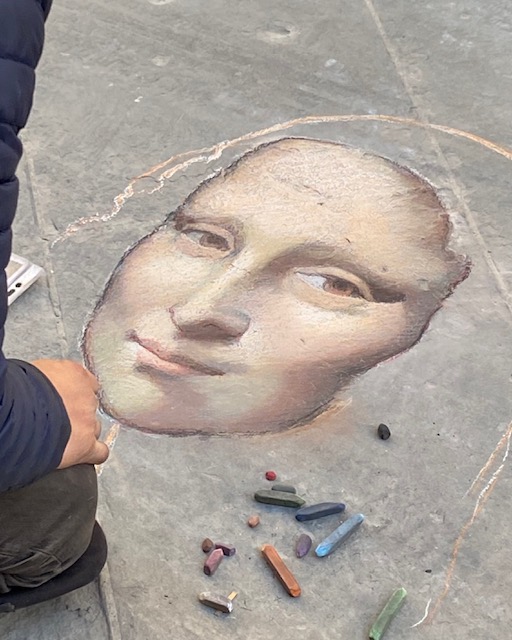 A sidewalk chalk artist works on a recreation of the Mona Lisa. Only the face is finished.