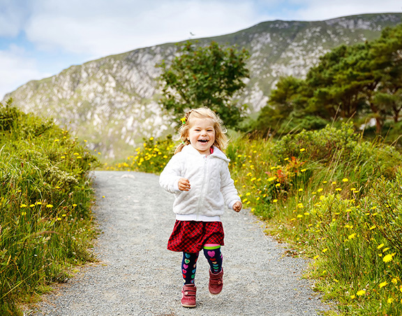 Cute little happy toddler girl running on nature path in Glenveagh national park in Ireland. Smiling and laughing baby child having fun spending family vacations in nature. Traveling with small kids.