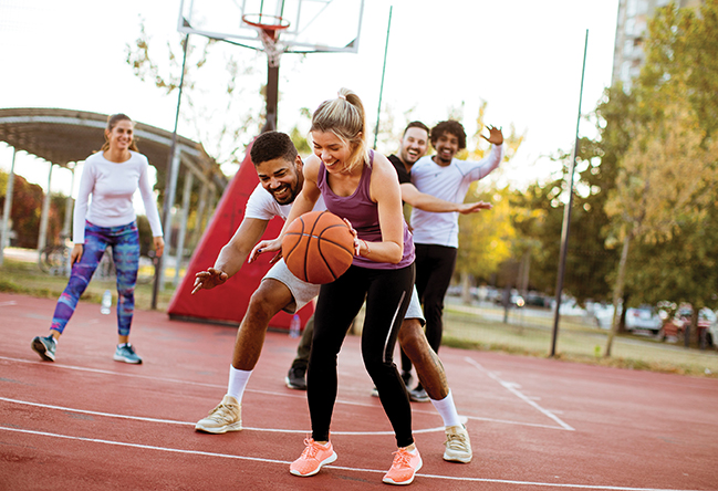 Group of multiracial young people playing basketball on court at outdoors