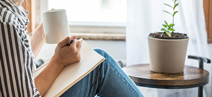 A young woman takes a break to do something analog like writing in her journal and drinking tea. This is a healthy practice for those who experience anxiety.
