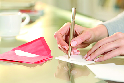 Close up of woman hand writing greeting thank you card sitting on a desk at home
