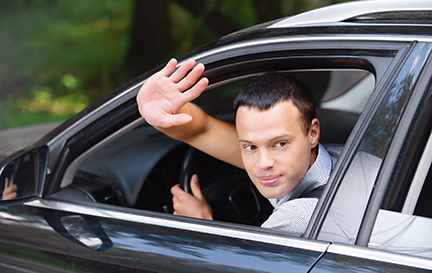 Portrait of young attractive handsome brunette man driving car and greeting somebody with hand.