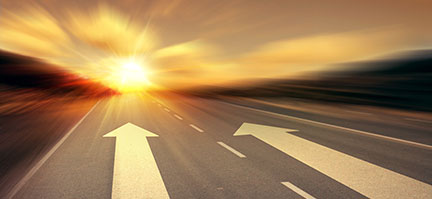 Arrows painted onto a highway road pointing away towards a setting sun