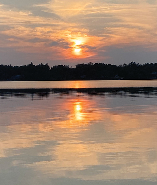 A beautiful orange and blue sunset over a body of water. The horizon is broken up by the silhouette of a forest.